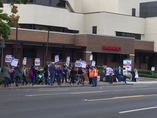 Workers march with signs in front of an ER entrance to a hosptial.