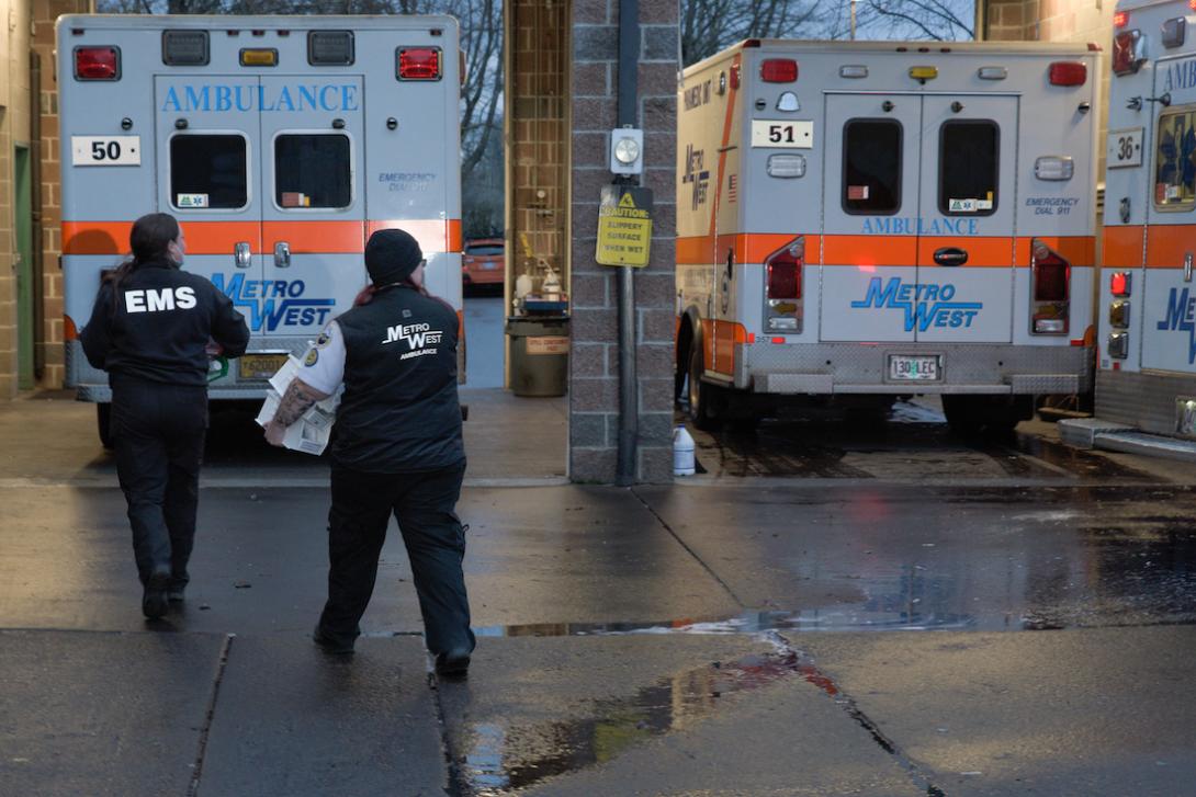 Metro West ambulance two people walk near ambulances bearing insignia for Metro West