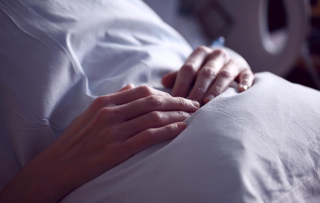 a white woman's hands clutch a pillow in a hospital bed