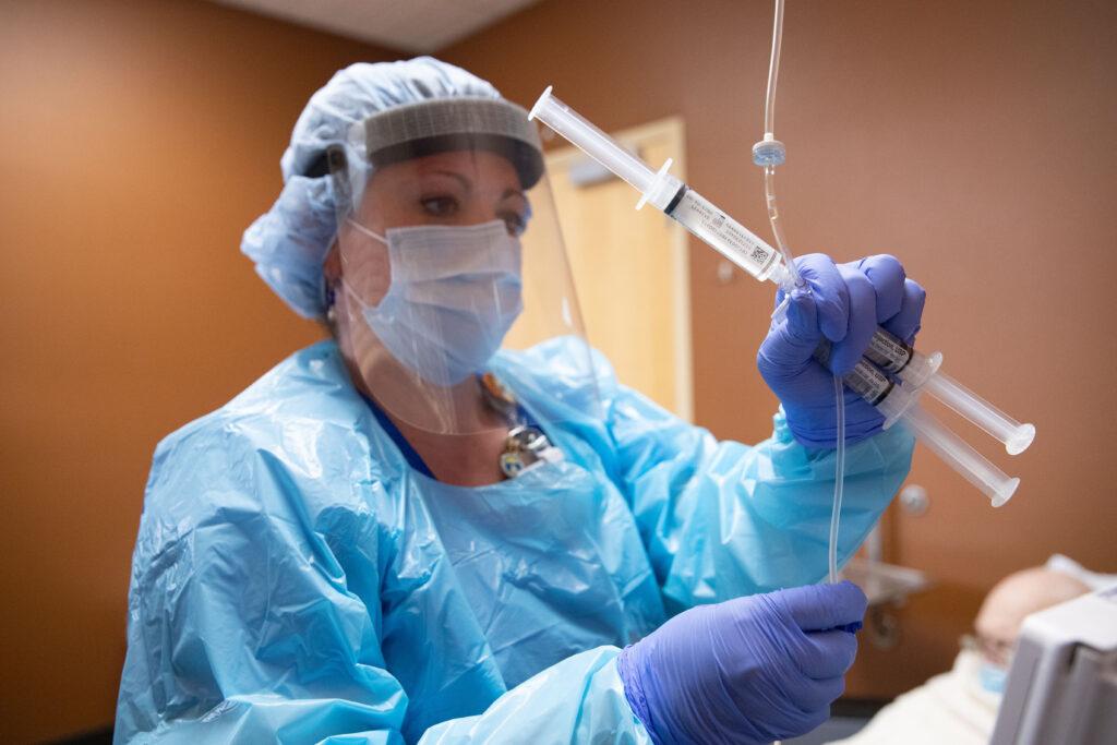 A health care worker in a face mask handles an IV tube in a hospital patient's room.