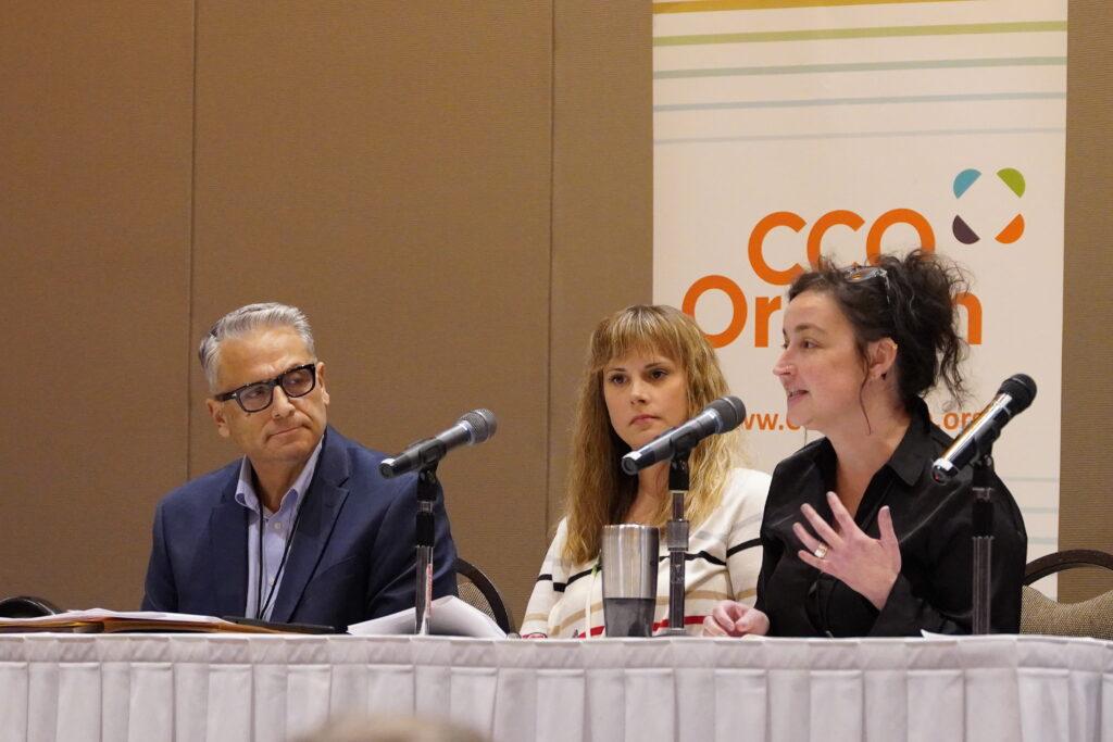 Three people sit at a table with microphones.