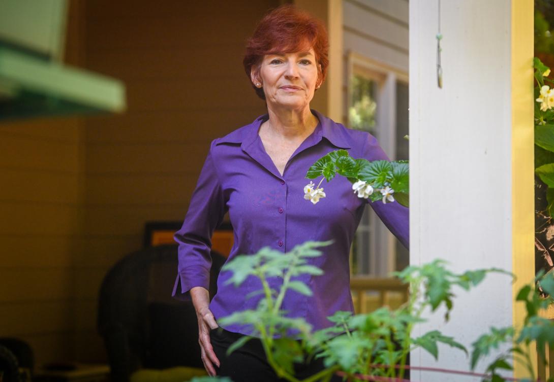 older woman stands on porch of house