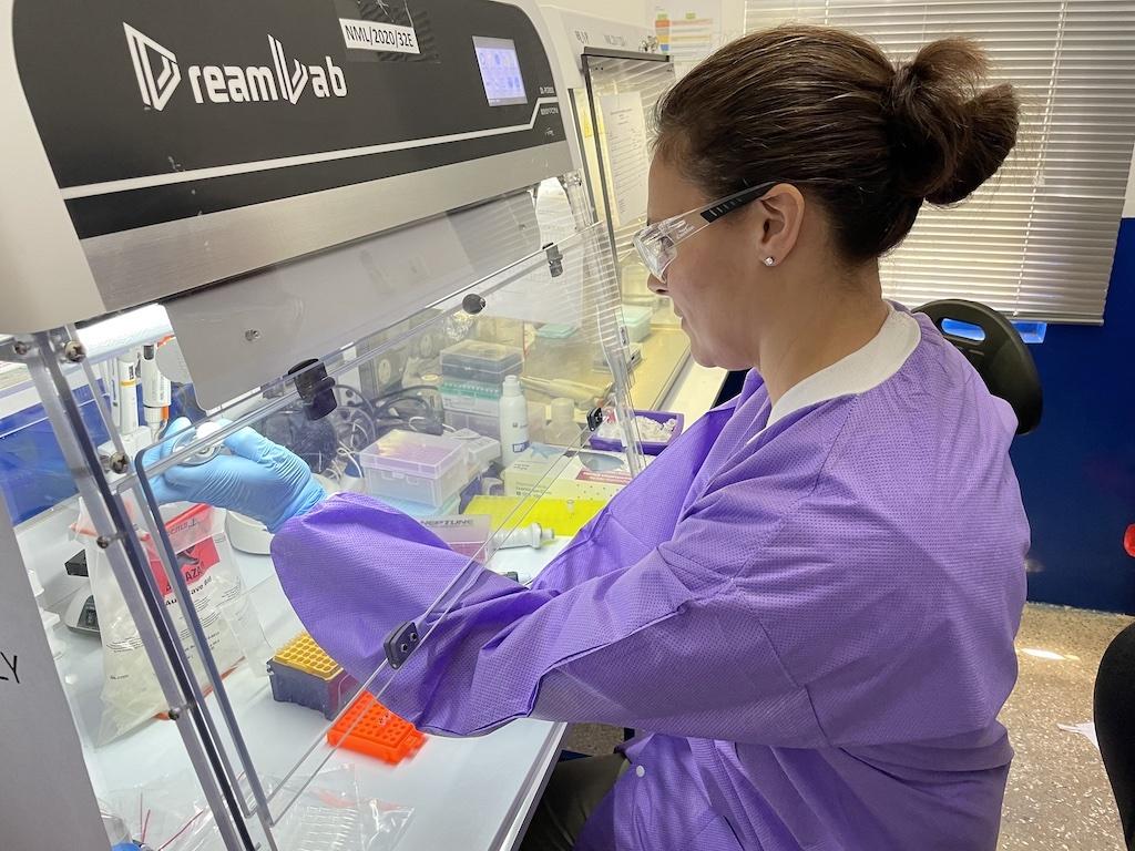 Nicolle Baird CDC woman in lab clothing and safety glasses works at research station