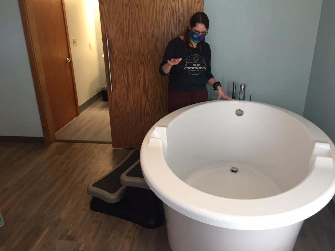 a woman stands next to a large porcelain tub used for birthing