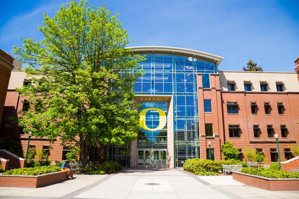 The exterior of a brick building on a spring day. Tall windows with the Oregon Ducks' O painted on the glass.