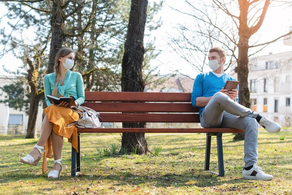 a woman and man sitting on a bench in a park with about 3 feet between them