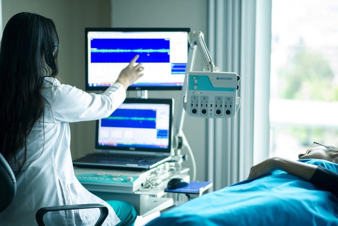 patient lies in bed next to a female medical worker who is examining a reading on a medical device.