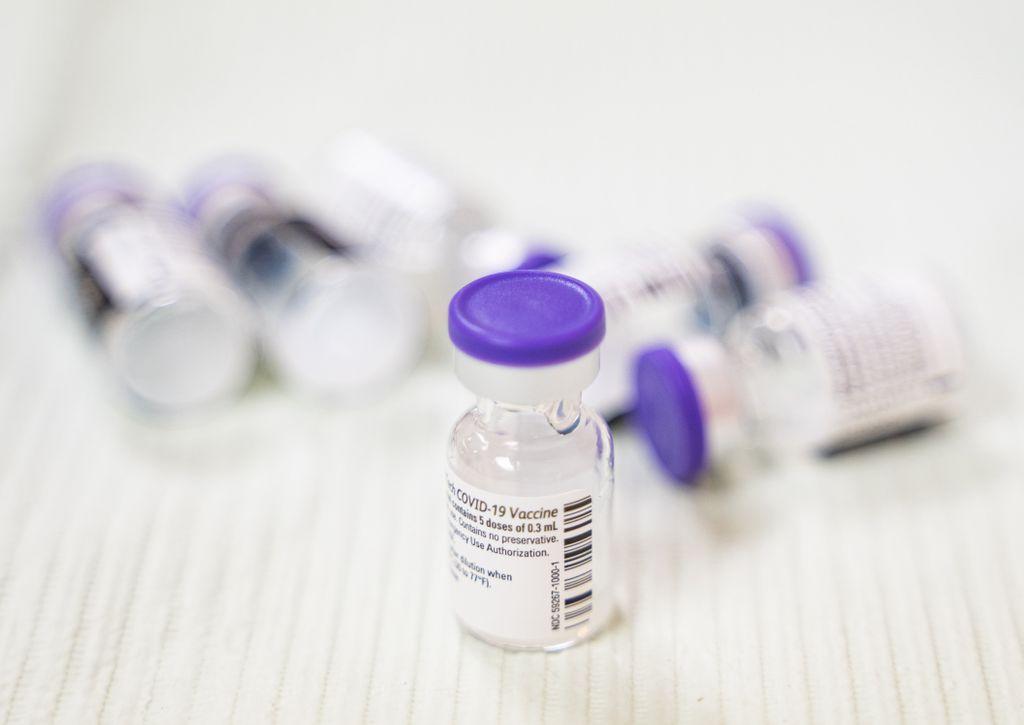 a close-up of pill bottles with purple caps and labels saying they contain covid-19 vaccine